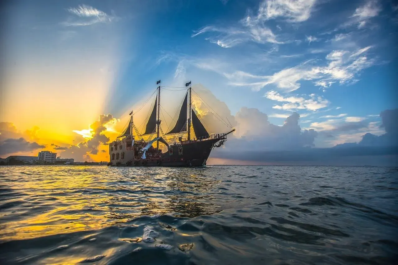 The Puerto Vallarta pirate ship under black sails on Banderas Bay as sun rays break through the clouds