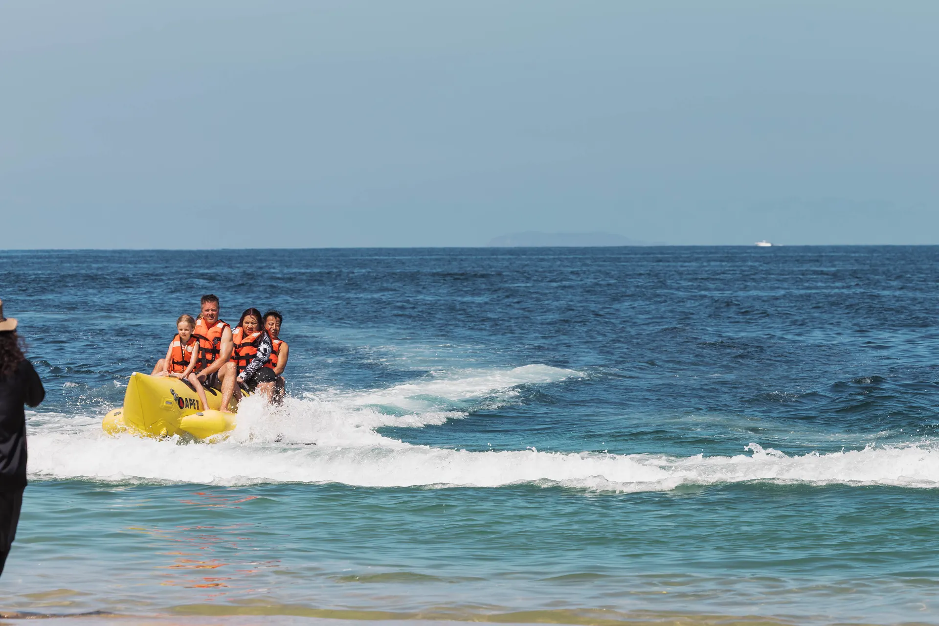 A family in life jackets riding a yellow banana boat through the surf on the day tour
