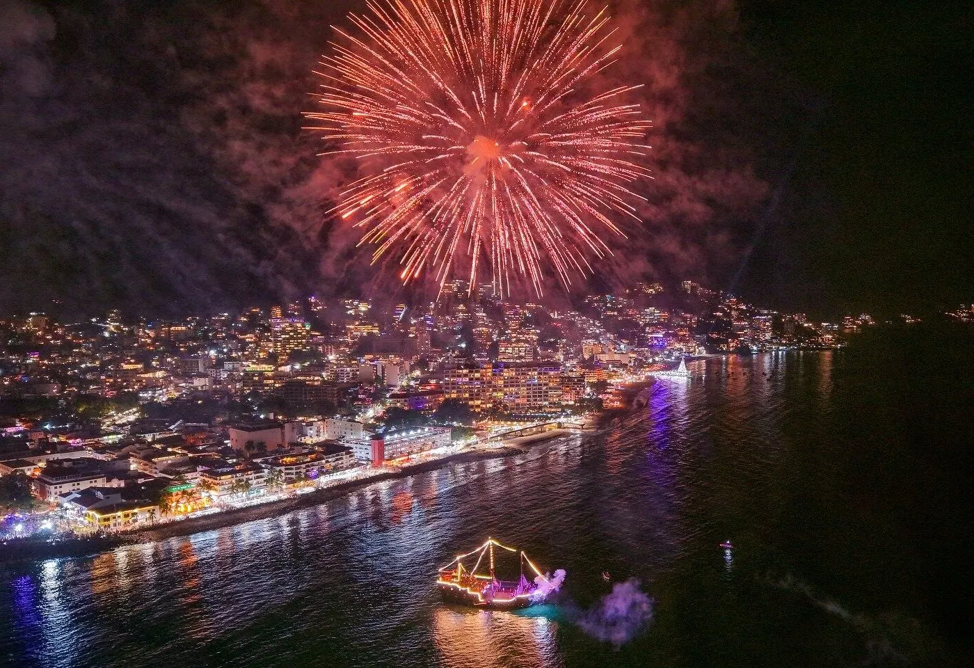 Fireworks burst over the Puerto Vallarta Malecon while the lit-up pirate ship sails the bay at night