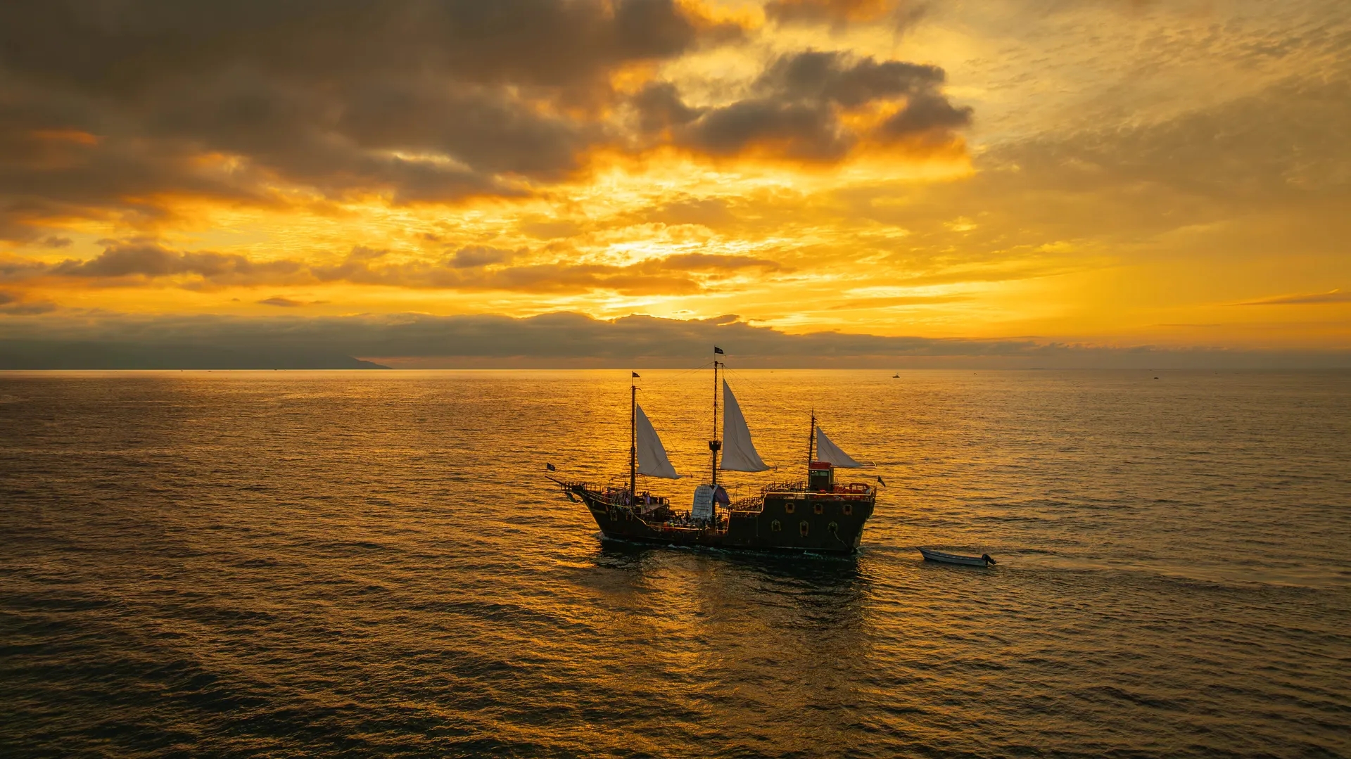 The Puerto Vallarta pirate ship under white sails on Banderas Bay at a golden sunset