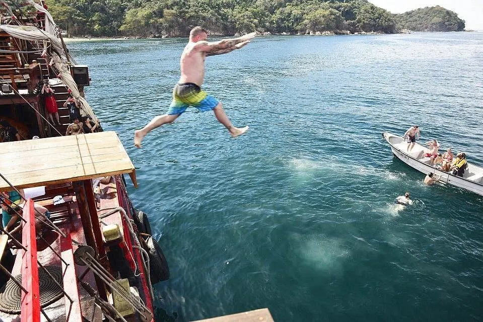 A guest leaps from the pirate ship into clear blue water near a jungle-covered shore