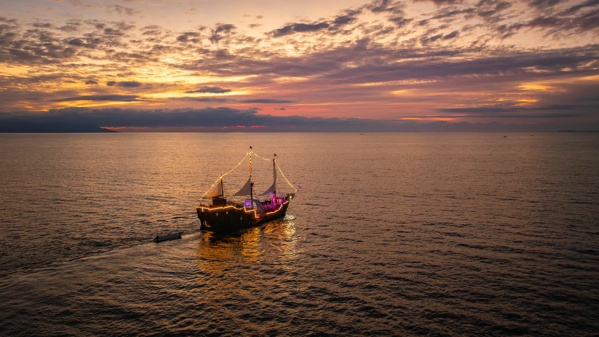 The pirate ship strung with lights heading out across Banderas Bay under a pink and orange dusk sky