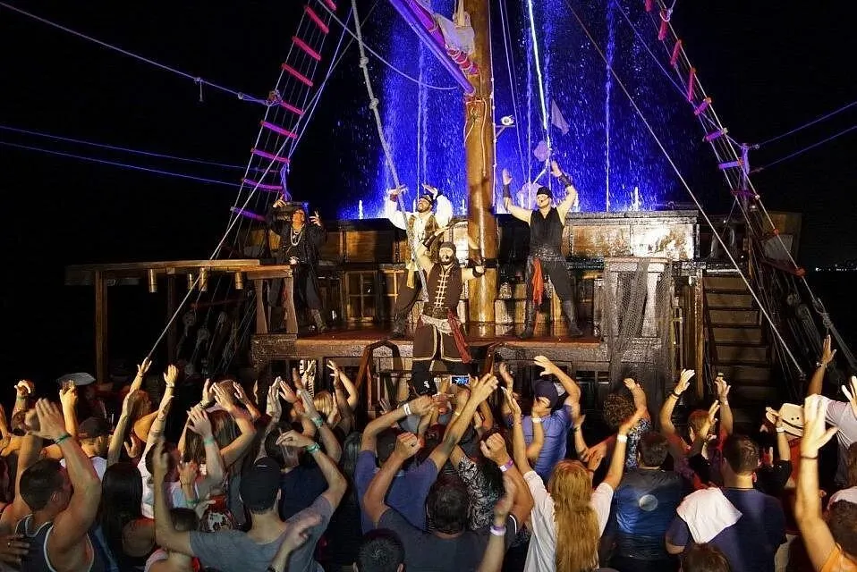 Guests cheer with raised arms as pirates perform on the upper deck during the night show