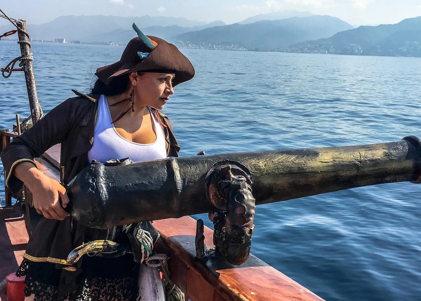 A pirate crew member mans a cannon at the rail, with the Puerto Vallarta mountains across the bay