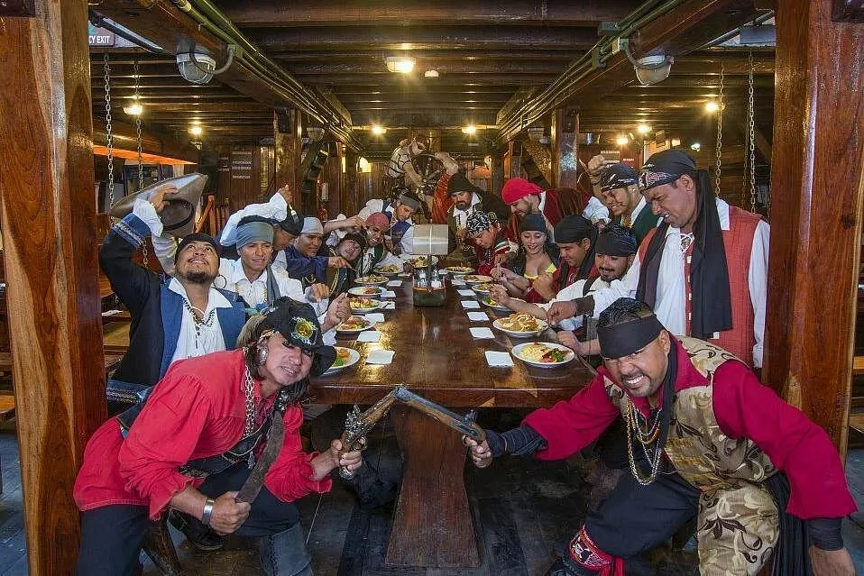The pirate crew gathered around a long wooden table of plated meals below deck