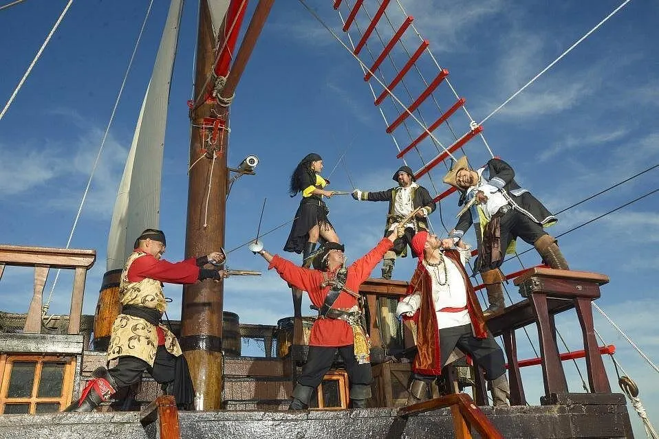 Costumed pirates stage a sword fight on deck beneath the rigging on a sunny day