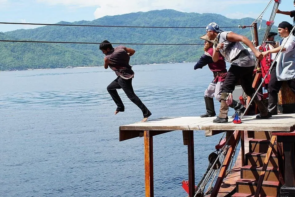 A pirate takes a running jump off the plank while the crew cheers him on
